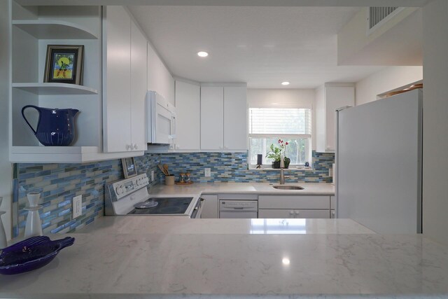 kitchen with a sink, light stone counters, white cabinetry, white appliances, and decorative backsplash