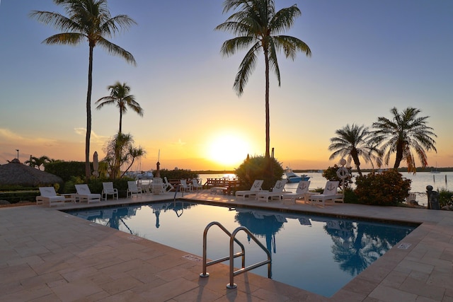 pool at dusk featuring a patio and a community pool