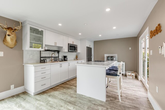 kitchen featuring a kitchen bar, a center island, stainless steel appliances, decorative backsplash, and white cabinets