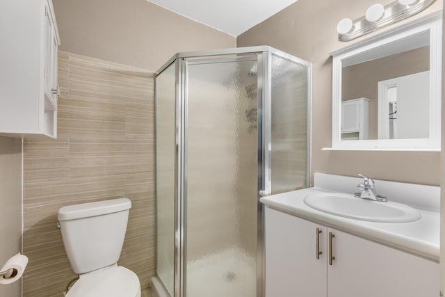 bathroom featuring walk in shower, vanity, toilet, and tile walls