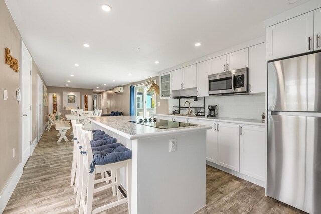 kitchen featuring a kitchen island, appliances with stainless steel finishes, a breakfast bar, white cabinets, and hardwood / wood-style flooring