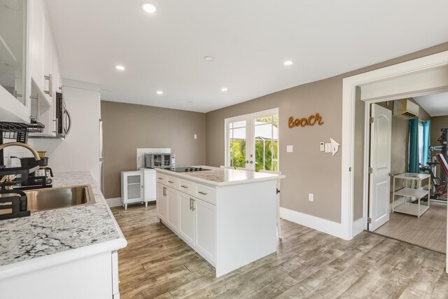 kitchen featuring sink, white cabinetry, a wall mounted air conditioner, a center island, and light hardwood / wood-style flooring