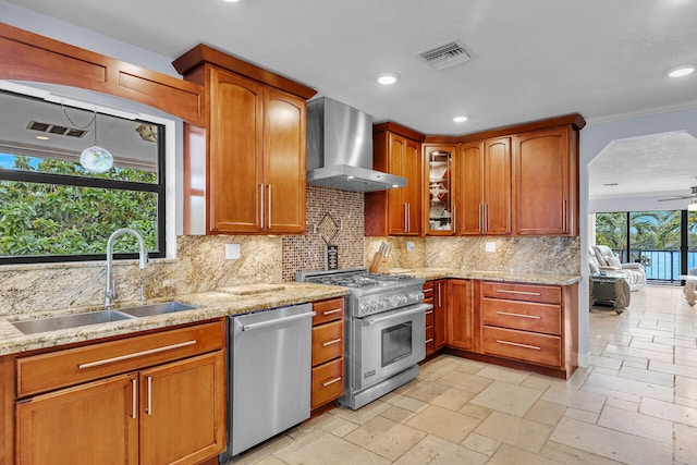 kitchen featuring wall chimney range hood, stainless steel appliances, sink, and light stone countertops