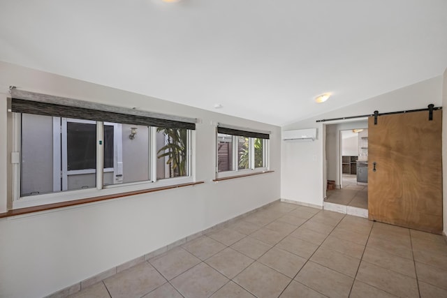 empty room with a wall mounted air conditioner, a barn door, baseboards, vaulted ceiling, and light tile patterned flooring