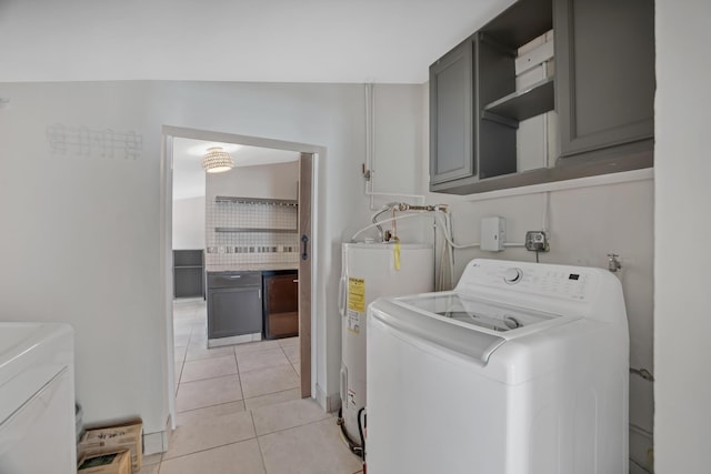 clothes washing area with cabinet space, water heater, light tile patterned floors, and washing machine and dryer