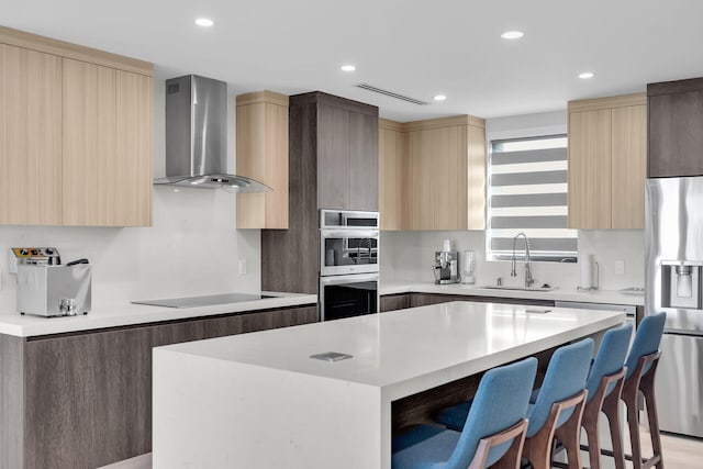 kitchen featuring sink, a breakfast bar area, appliances with stainless steel finishes, a kitchen island, and wall chimney range hood