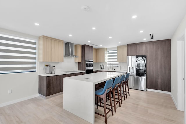 kitchen with a sink, a breakfast bar area, wall chimney exhaust hood, a center island, and stainless steel appliances