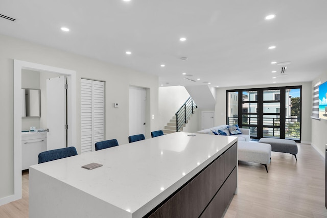 kitchen featuring french doors, a breakfast bar area, light stone counters, light wood-type flooring, and a large island