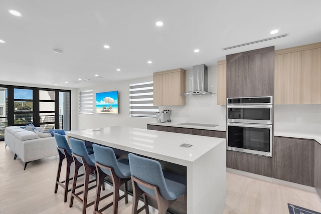 kitchen with a kitchen breakfast bar, wall chimney exhaust hood, a healthy amount of sunlight, a kitchen island, and stainless steel double oven