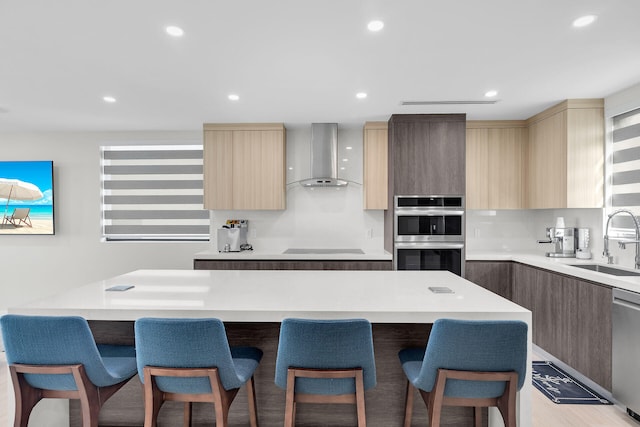 kitchen featuring sink, stainless steel appliances, a center island, a kitchen bar, and wall chimney exhaust hood