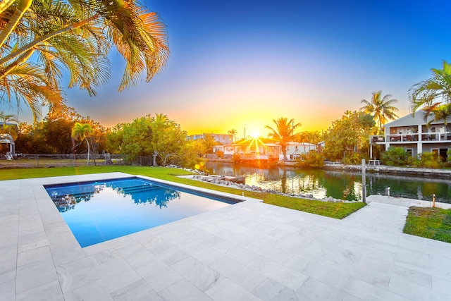 pool at dusk featuring a water view and a patio area