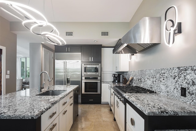 kitchen featuring exhaust hood, built in appliances, decorative light fixtures, an island with sink, and white cabinets