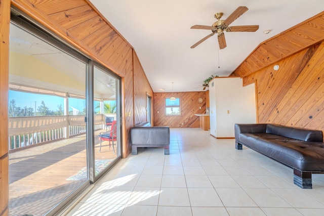 living room with ceiling fan, lofted ceiling, light tile patterned floors, and wooden walls