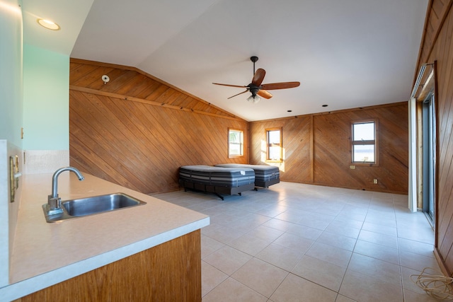 interior space featuring sink, light tile patterned floors, ceiling fan, wooden walls, and vaulted ceiling