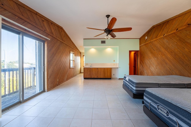 unfurnished bedroom with wooden walls, lofted ceiling, access to outside, light tile patterned floors, and ceiling fan