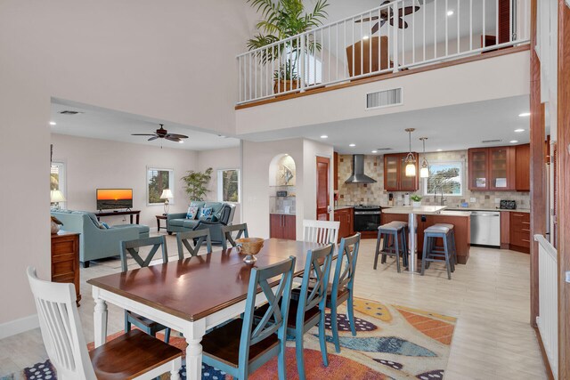 dining area with ceiling fan, light wood-type flooring, and a high ceiling