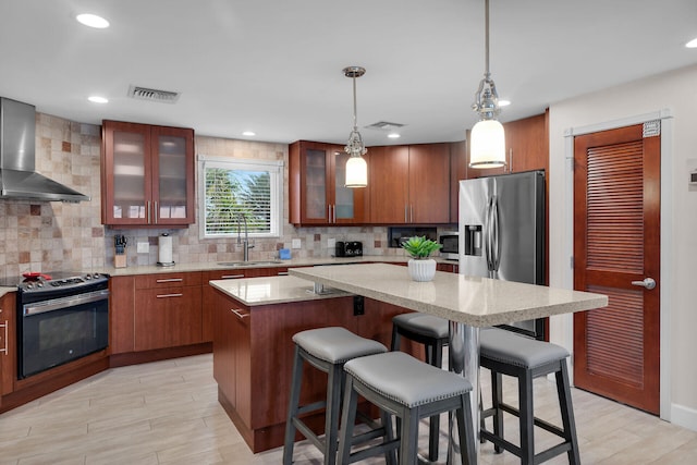 kitchen featuring sink, a center island, pendant lighting, stainless steel appliances, and wall chimney range hood