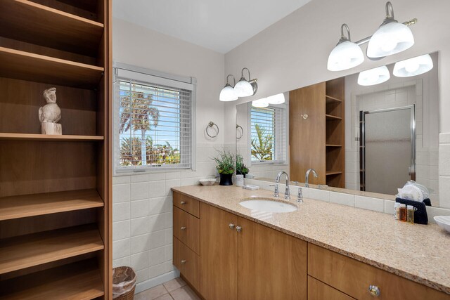 bathroom with a shower with door, vanity, tile walls, and tile patterned floors