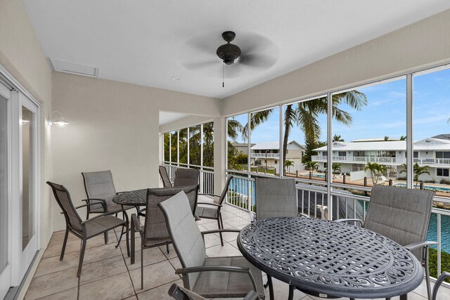 sunroom with ceiling fan and a water view