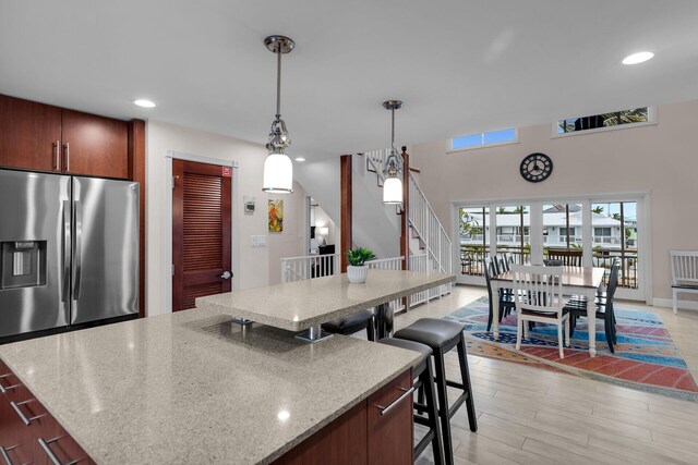 kitchen with pendant lighting, stainless steel fridge, a spacious island, light stone counters, and light wood-type flooring