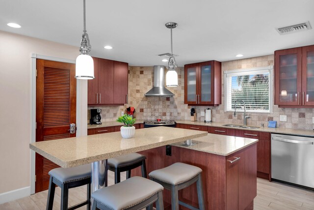 kitchen with wall chimney exhaust hood, sink, appliances with stainless steel finishes, a kitchen island, and pendant lighting