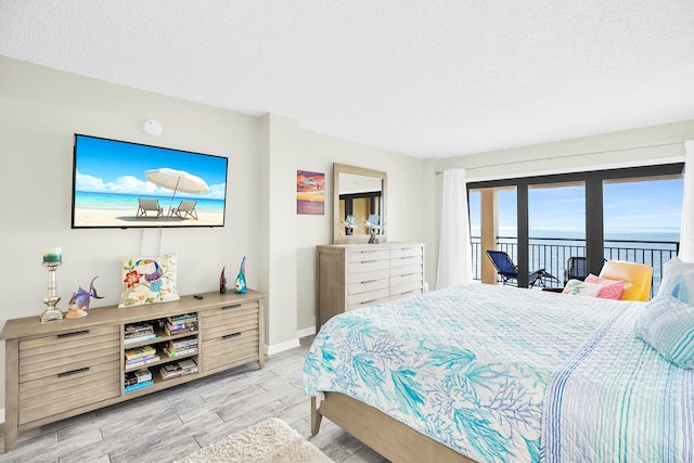 bedroom featuring access to exterior, a textured ceiling, and a water view