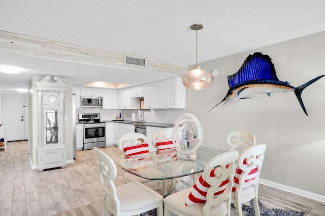 dining room with sink, a textured ceiling, and light wood-type flooring