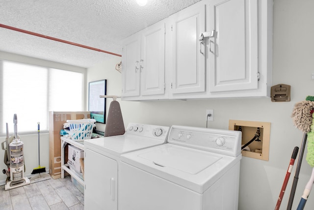 washroom featuring cabinets, light hardwood / wood-style flooring, a textured ceiling, and washing machine and clothes dryer