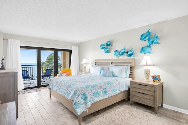 bedroom featuring light wood-type flooring, access to outside, a textured ceiling, and a water view