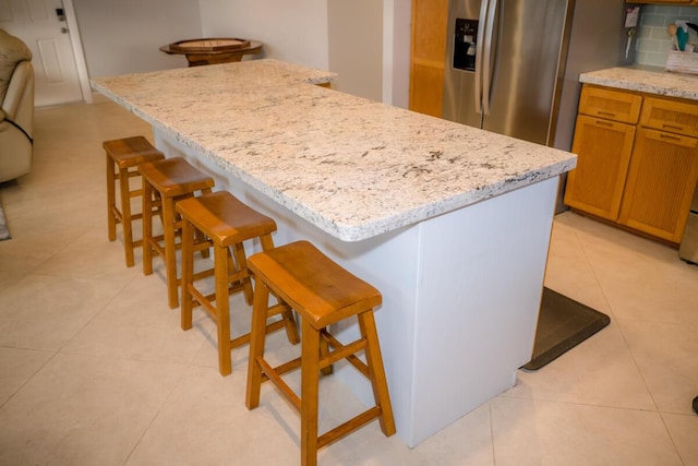 kitchen with tasteful backsplash, brown cabinetry, a kitchen island, a breakfast bar area, and stainless steel refrigerator with ice dispenser