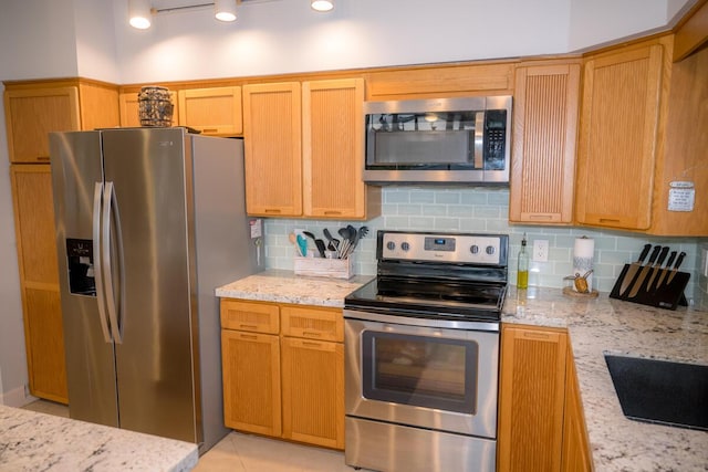 kitchen with stainless steel appliances, light tile patterned floors, decorative backsplash, and light stone countertops