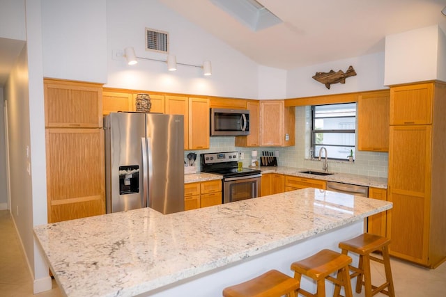 kitchen with stainless steel appliances, a sink, visible vents, tasteful backsplash, and a kitchen bar