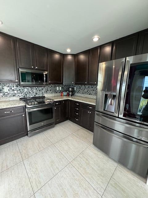 kitchen with dark brown cabinetry, backsplash, light tile patterned floors, and stainless steel appliances