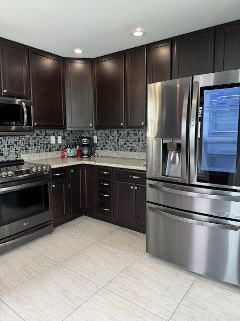 kitchen with appliances with stainless steel finishes, dark brown cabinets, light stone counters, and decorative backsplash