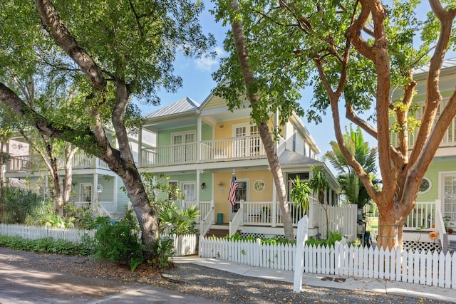 view of front facade featuring a balcony, a fenced front yard, metal roof, covered porch, and a gate