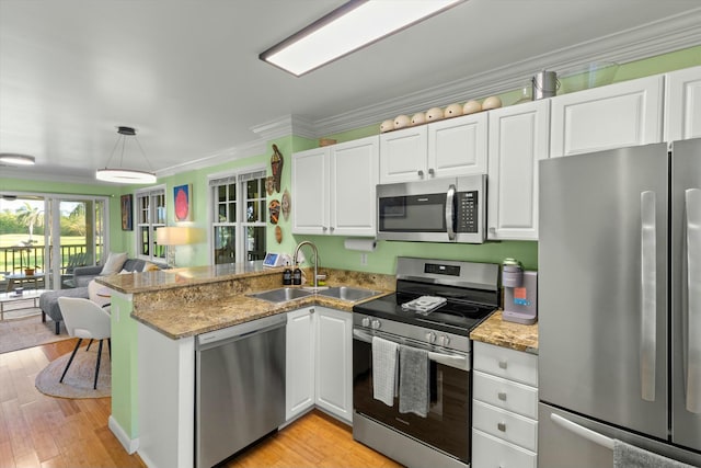 kitchen featuring stainless steel appliances, ornamental molding, open floor plan, a sink, and a peninsula