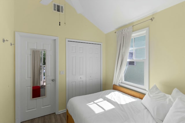 bedroom with lofted ceiling, a closet, visible vents, and wood finished floors