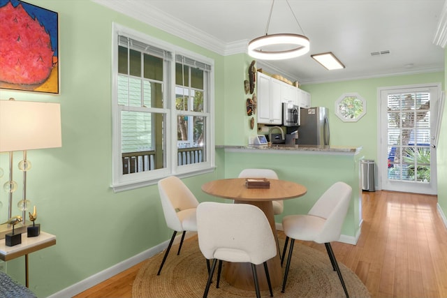 dining space with ornamental molding, light wood-type flooring, visible vents, and baseboards