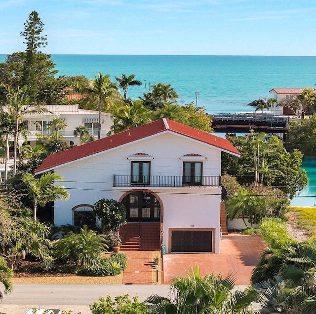 view of front of property featuring french doors, stucco siding, a water view, a balcony, and a garage