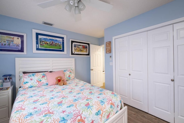 bedroom with a ceiling fan, wood finished floors, visible vents, and a closet