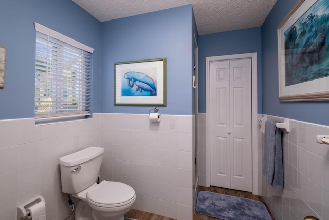 bathroom with a wainscoted wall, a closet, a textured ceiling, tile walls, and toilet