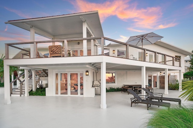 back house at dusk with a balcony, a patio area, and french doors