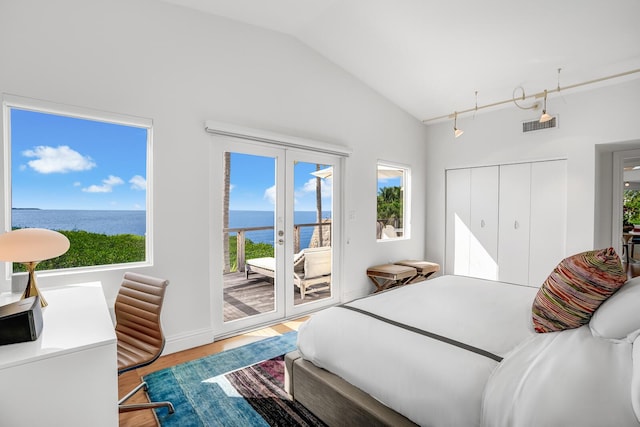 bedroom with vaulted ceiling, hardwood / wood-style floors, a water view, access to outside, and french doors