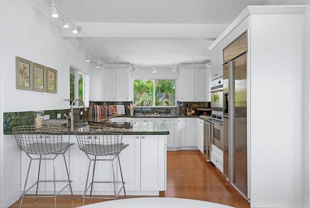 kitchen featuring wall oven, backsplash, kitchen peninsula, and white cabinets