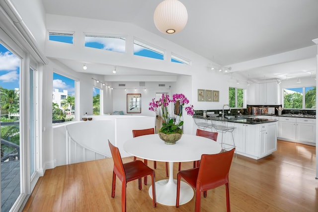 dining space featuring high vaulted ceiling, sink, and light wood-type flooring