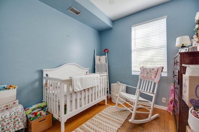 bedroom featuring ceiling fan, a nursery area, and light hardwood / wood-style floors