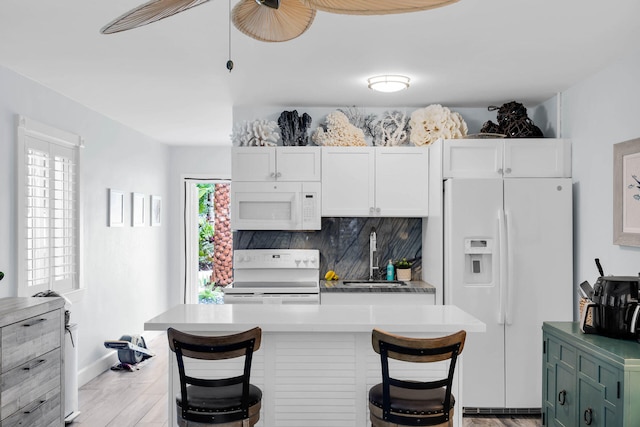 kitchen featuring a breakfast bar, white cabinetry, sink, decorative backsplash, and white appliances