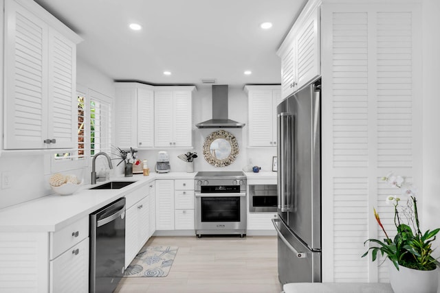 kitchen with sink, white cabinets, premium appliances, light hardwood / wood-style floors, and wall chimney range hood