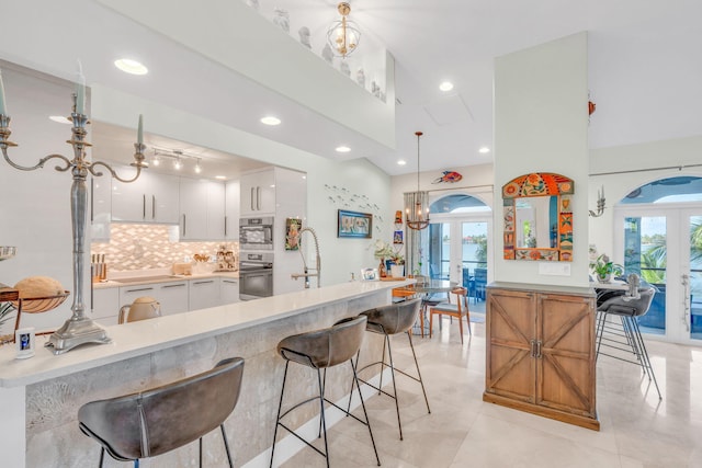 kitchen with a breakfast bar, pendant lighting, white cabinetry, backsplash, and french doors