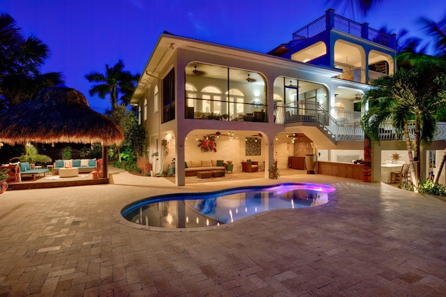 back house at night featuring ceiling fan, a patio area, outdoor lounge area, and a balcony